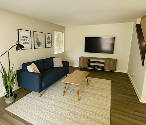 A living room with a blue couch, a wooden coffee table, and a flat screen TV mounted on the wall.