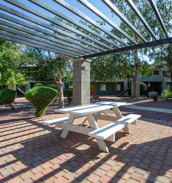 A white picnic table is in the middle of a brick patio.