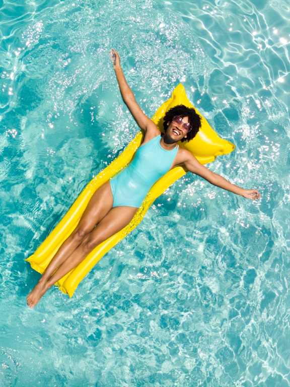 A woman in a blue swimsuit is floating on a yellow float in a pool.