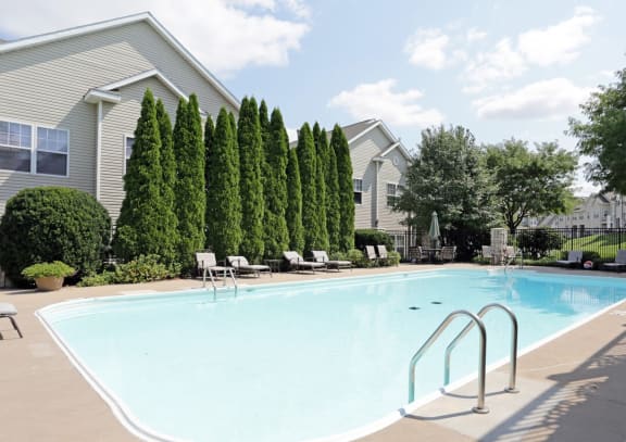 a large swimming pool with chaise lounge chairs and trees in the background