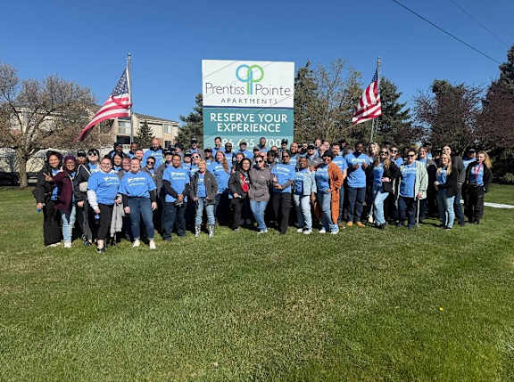 A group of people in blue shirts stand in front of a Prentice Pointe Apartments sign.