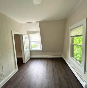 a bedroom with hardwood floors and two windows