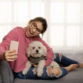 a woman sitting on a couch holding a dog and looking at a cell phone