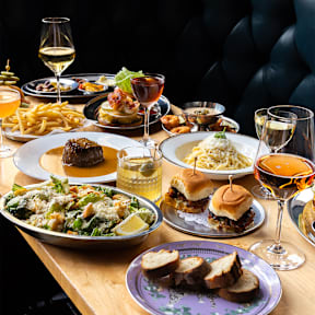 A variety of dishes are served on a table with wine glasses.