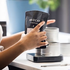 A person is holding a black packet of MadCap Coffee.