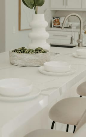 A white kitchen with a basket of green leaves on the counter.