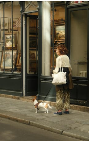 A woman walking her dog in front of a shop.