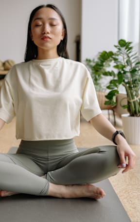 A person is sitting cross-legged on a yoga mat in a room.