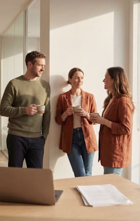 Three people are standing in a room with a laptop and papers on the table.