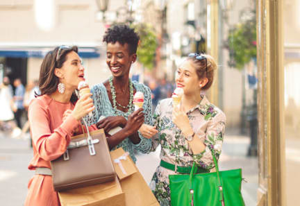 Three women are standing on a street, one of them is holding a green bag.