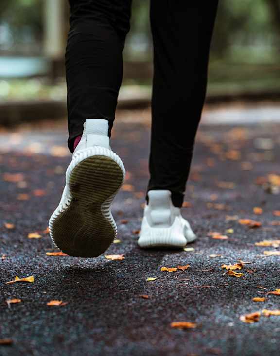 A person is walking on a path with leaves on the ground.