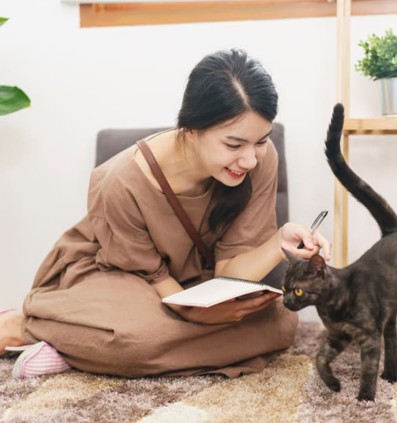 a woman sitting on the floor with a cat and writing in a notebook