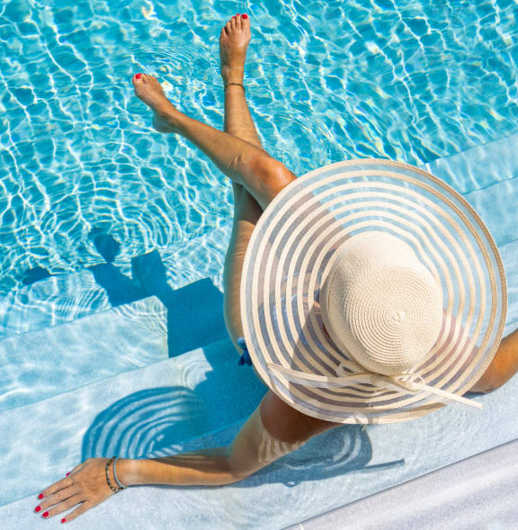 a woman in a floppy hat sitting on the side of a pool
