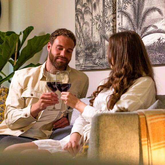 A man and a woman are sitting on a couch, each holding a glass of wine.