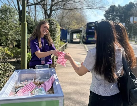 A woman in a purple shirt is handing out pink packets to another woman.
