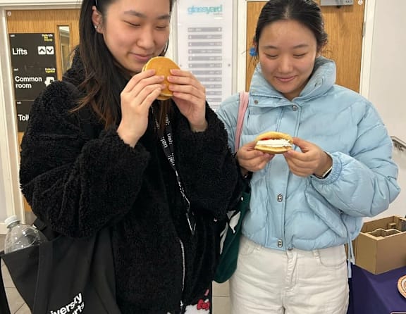 Two women eating sandwiches in front of a sign that says "Lifts".