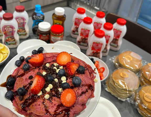 A plate of pancakes topped with strawberries, blueberries, chocolate chips, and syrup.