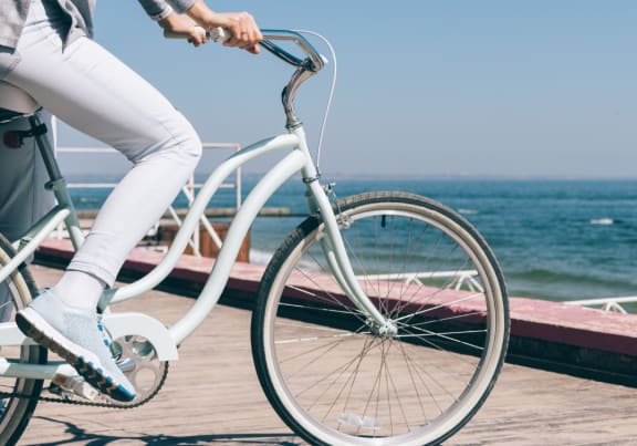 a woman riding a bike on a boardwalk with the ocean in the background
