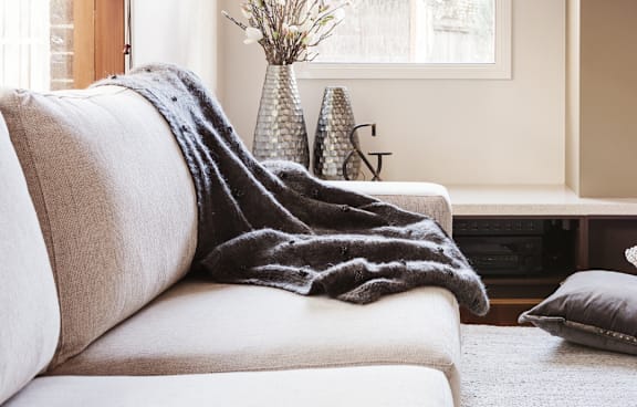 A white couch with a grey blanket on it.