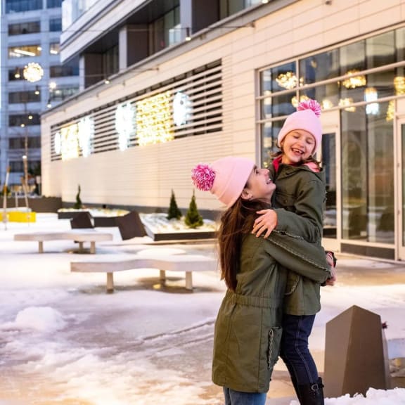 a mother and daughter smile at each other while standing in the snow in front of a building