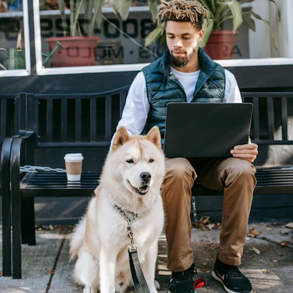 a man sitting on a bench with a dog and his laptop at Rivers Landing Apartments, PRG Real Estate, Hampton, Virginia