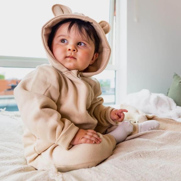 a baby sitting on a bed wearing a teddy bear costume