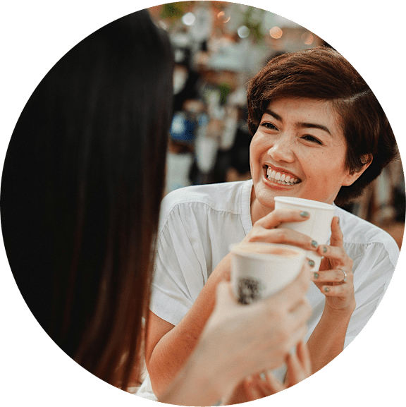 A woman is holding a cup of coffee and talking to another person.