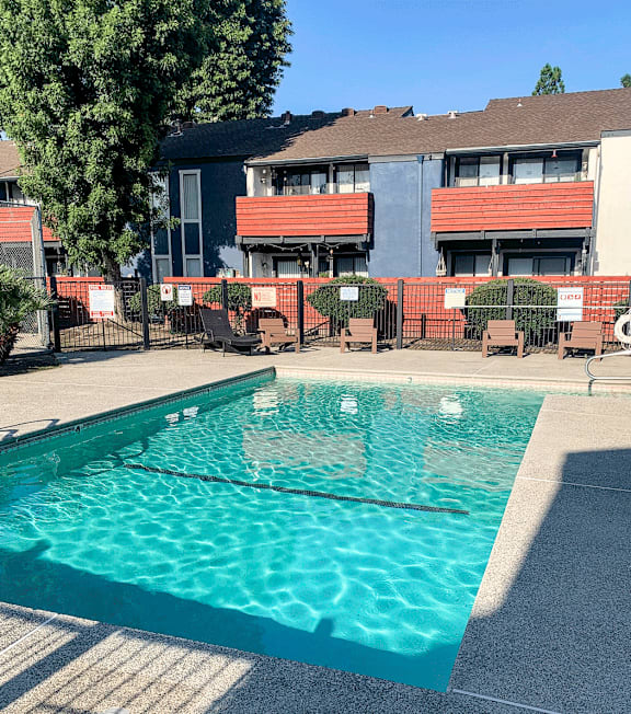 A swimming pool in front of a building with red and grey balconies.