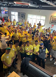 A group of people wearing yellow shirts are gathered in a room.