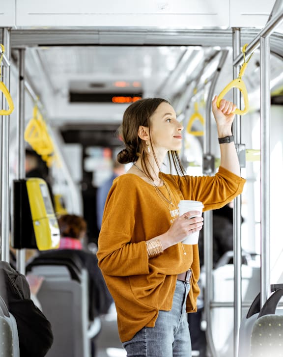 A woman in a yellow top is holding onto a yellow handbar while standing on a bus.