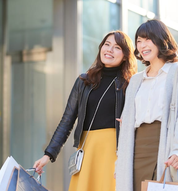Two women holding shopping bags in front of a store window.