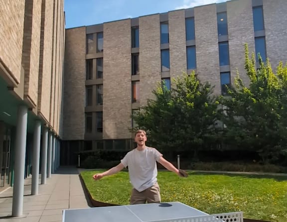 A man is playing ping pong in a sunny outdoor area.