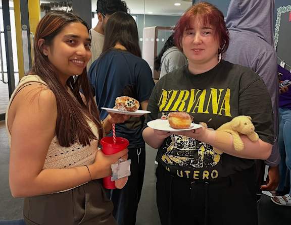 A woman in a Nirvana t-shirt holds a plate with a donut and a stuffed animal.