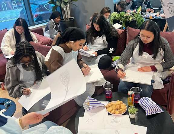 A group of people sitting around a table, working on papers and eating snacks.