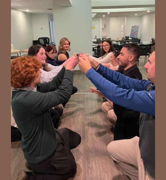 A group of people sitting on the floor in a circle holding hands.