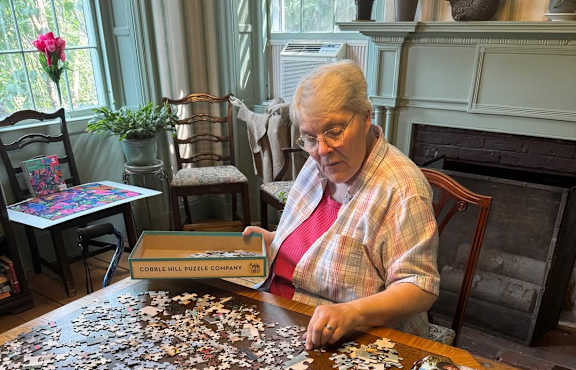A woman is sitting at a table and working on a puzzle.