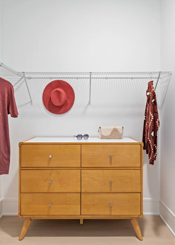 A wooden chest of drawers with a red hat and sunglasses on top.