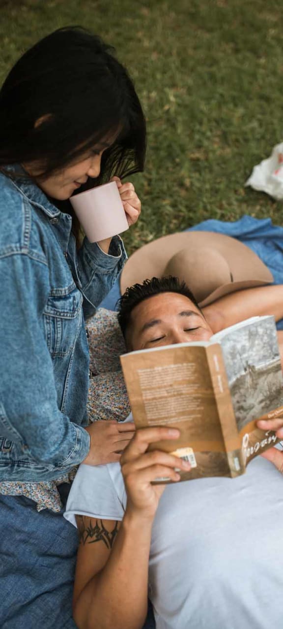 a couple lying on the grass reading a book and drinking coffee