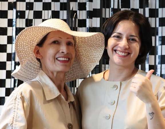 Two people wearing hats and light-colored clothing are standing in front of a black and white checkered floor.