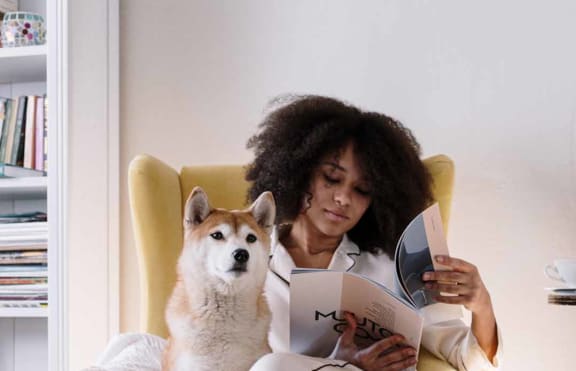 a woman sitting in a yellow chair reading a book with her dog sitting on her lap