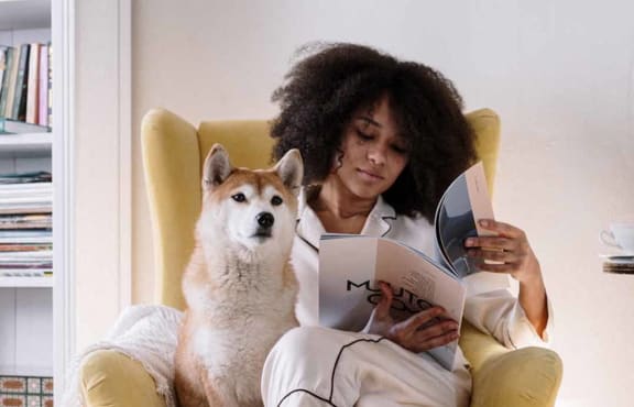 a woman sitting in a chair with her dog reading a book