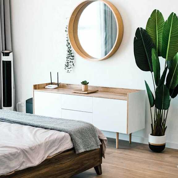 A bedroom with a bed, a mirror, and a plant.
