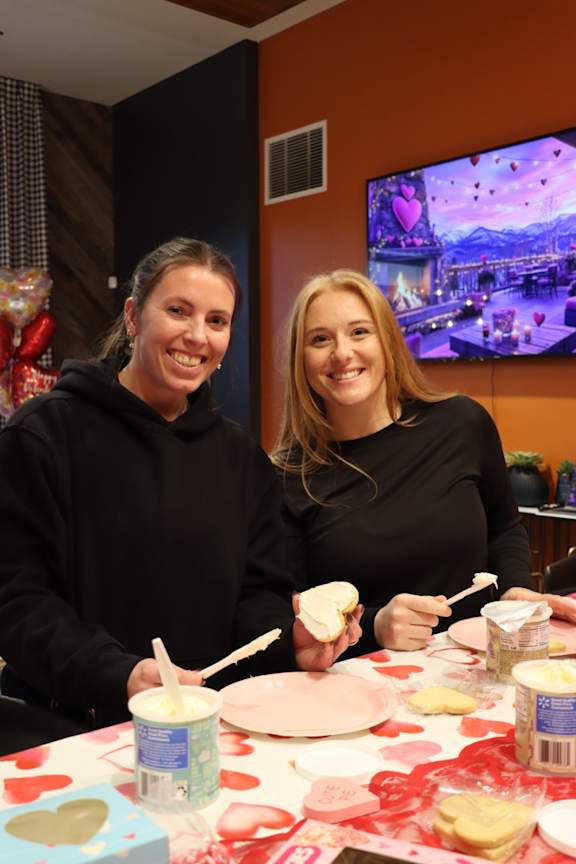 Two women are standing in front of a table with various items on it.