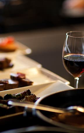 A glass of red wine is on a table next to a plate of food.