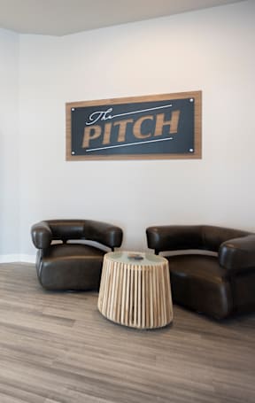 Two black leather chairs and a round table in front of a sign that says "The Pitch".