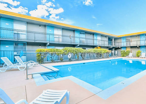 A swimming pool is surrounded by lounge chairs in front of a building.