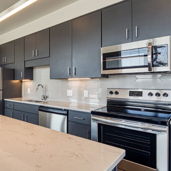 an empty kitchen with black cabinets and a white counter top