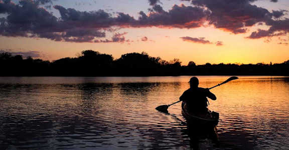 a man paddling a canoe on a lake at sunset