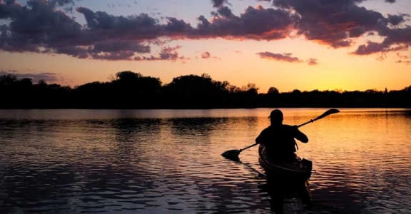 a man paddling a canoe on a lake at sunset