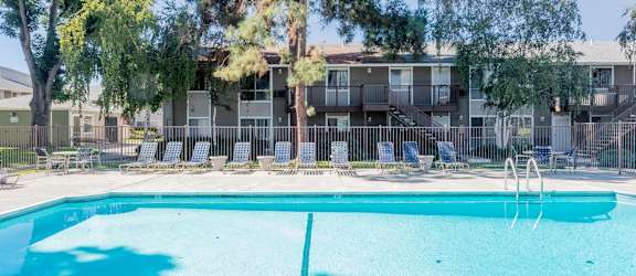 A swimming pool in front of a building with trees and chairs around it.
